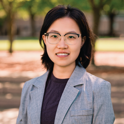 Xin (Zoe) Zhou standing outside on a sunny day for a headshot.